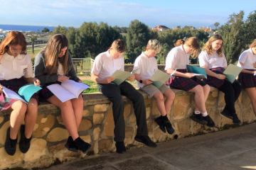 Children sitting on a wall reading