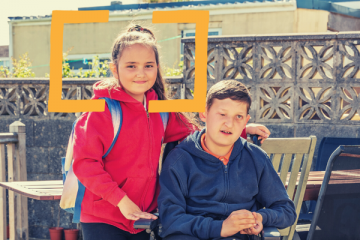 Young girl standing next to a boy in a wheelchair