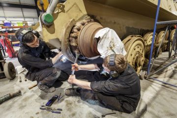 Young apprentices work on the wheels of a military tank at The Tank Museum