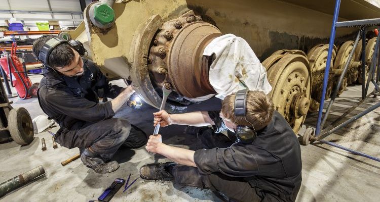Young apprentices work on the wheels of a military tank at The Tank Museum